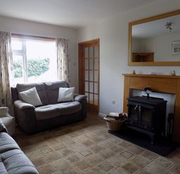 A living room with sofas a fireplace with wood burner and mirror above at Brookfield in St Gennys near Wainhouse Corner