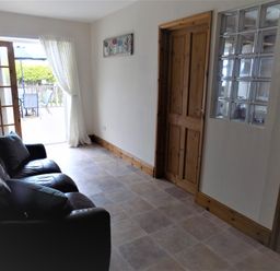 A room with a black leather sofa next to a wooden door and glass block window at Brookfield in St Gennys near Wainhouse Corner
