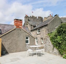 An outdoor patio with a white metal table and four chairs surrounded by stone buildings and greenery at 10 Westgate Hill in Pembroke