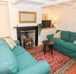 A living room with two green sofas a red patterned rug a wood burning stove and a small black round table at 10 Westgate Hill in Pembroke
