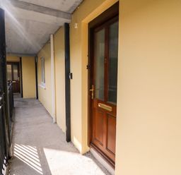 An outdoor corridor with yellow walls and brown wooden doors at 2 Garnish Court in Glengarriff County Cork