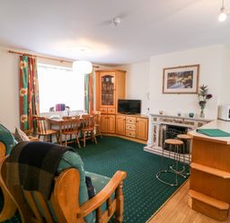 A living room with wooden chairs a dining table television fireplace and a microwave at 2 Garnish Court in Glengarriff County Cork