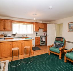 A kitchen with wooden cabinets and stools next to a living area with two green cushioned armchairs at 2 Garnish Court in Glengarriff County Cork