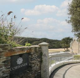 A stone wall with a corisande sign and a driveway leading to a building near the beach at The Tower 5 Corisande Manor in Newquay