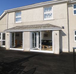 A house exterior with open bi-fold doors leading to a wooden deck at Estuary View in Newton Ferrers