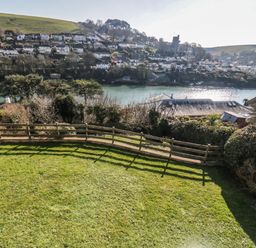 A grassy backyard with a wooden fence overlooking a river and a hillside with houses at Estuary View in Newton Ferrers