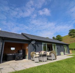 A patio area with outdoor seating and a hot tub attached to a single-story house in a rural setting at Dol Blodau in Newbridge-On-Wye