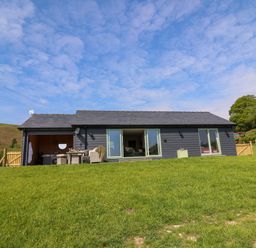 A single story house with patio furniture on a grassy hill at Dol Blodau in Newbridge-On-Wye