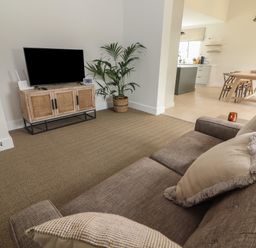 A living room with a brown sofa facing a television on a wooden cabinet with a potted plant next to it and a dining area with a wooden table and chairs in the background at Shannon Vale in Woodford County Galway