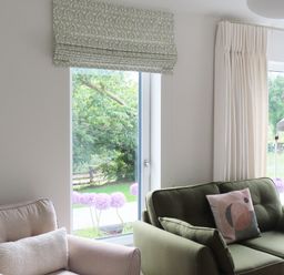 A living room with a beige armchair and a green sofa next to large windows with patterned and plain curtains at Shannon Vale in Woodford County Galway