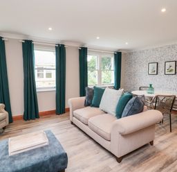A living room with a beige sofa, armchair, ottoman, dining table, chairs, and green curtains at 2 Apple Tree in Beadnell