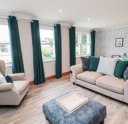 A living room with a beige sofa and armchair with teal curtains at 2 Apple Tree in Beadnell