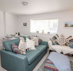 A living room with a teal sofa and white armchair with patterned cushions and a dining table at Lane Cottage in Cardigan