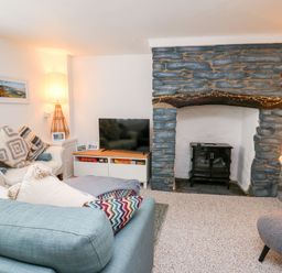 A living room with a stone fireplace a wood stove a television on a cabinet sofas with cushions a floor lamp and a lantern at Lane Cottage in Cardigan
