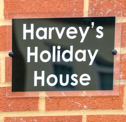 A black sign with white text reading Harveys Holiday House mounted on a red brick wall at Harveys Holiday House in Hunstanton