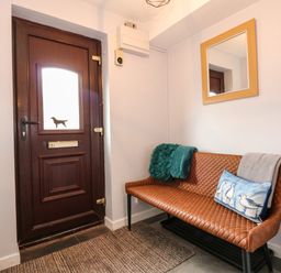 An entryway with a brown door with a dog silhouette on the window and a brown bench with cushions and a mirror on the wall at Harveys Holiday House in Hunstanton