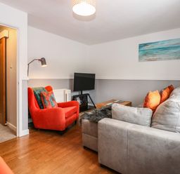 A living room with a gray sofa and an orange armchair a wooden floor and a painting on the wall at Harveys Holiday House in Hunstanton