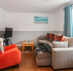 A living room with a gray sofa and orange armchair a wooden coffee table and a wall-mounted TV at Harveys Holiday House in Hunstanton