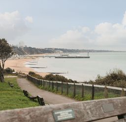 A coastal walkway with benches overlooking a sandy beach and a pier at The Anchorage in Bournemouth