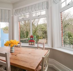 A dining area with a wooden table and white chairs near windows and a vase with yellow flowers at The Anchorage in Bournemouth