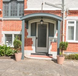 An entrance door with glass panels under a porch with two potted plants on each side at The Anchorage in Bournemouth