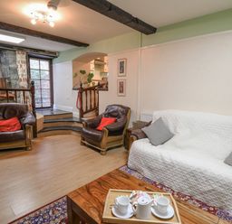 A living room with leather armchairs and a sofa covered with a white throw and a wooden coffee table with a tea set at The Searle in Nantmel near Rhayader