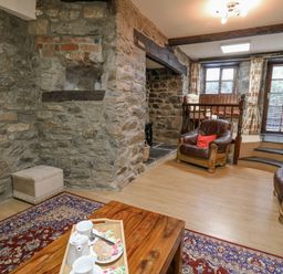 A living room with stone walls, leather chairs, a wooden table with tea set and a rug at The Searle in Nantmel near Rhayader