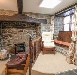 A stone walled room with a fireplace a leather armchair an upholstered armchair and a window seat with cushions at The Searle in Nantmel near Rhayader