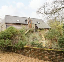 A wooden house with a staircase surrounded by bushes and a statue in a garden at Avon Turn View in Alderbury