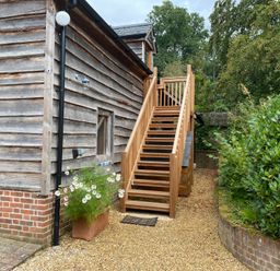 An exterior wooden staircase next to a wooden building with a brick base and a planter with flowers at Avon Turn View in Alderbury