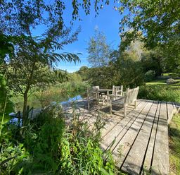A wooden deck with chairs and a table next to a pond surrounded by trees and greenery at Avon Turn View in Alderbury