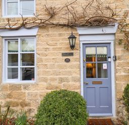 The front view of a stone house with a blue door and two windows with bushes in front at Riseholme in Ebberston
