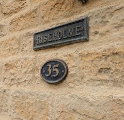 A stone wall with a sign reading Riseholme and a house number 35 plaque at Riseholme in Ebberston