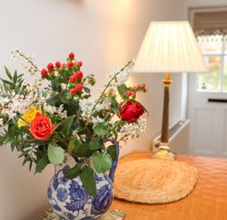 A table with a floral arrangement in a blue and white vase and a lamp near a white door at Riseholme in Ebberston