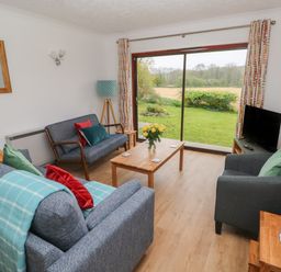A living room with blue sofas a wooden coffee table and a television near a large sliding glass door at Timaru in Lamphey