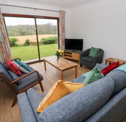 A living room with sofas chairs a coffee table and a television with a view of a garden at Timaru in Lamphey