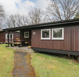 A brown wooden cabin with a picnic table on a concrete patio in front and a grassy yard at 64 Penlan Holiday Park Cenarth