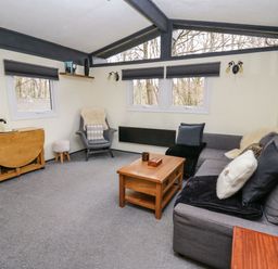A living room with a gray sofa a wooden coffee table an armchair with a sheepskin and a small wooden foldable table at 64 Penlan Holiday Park in Cenarth
