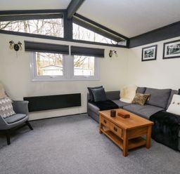 A living room with a gray sofa black pillows wooden coffee table gray armchair and windows with black blinds at 64 Penlan Holiday Park in Cenarth