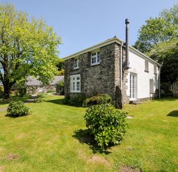 A stone and white house with garden shrubs and a tree at Byre in Trethin near Camelford