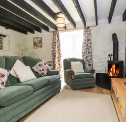 A living room with green sofa and armchair a wood burning stove and a television on a wooden stand at Byre Trethin near Camelford