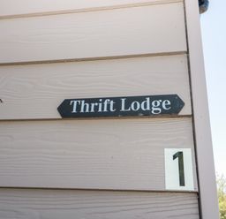 A sign on a beige wooden wall that says Thrift Lodge with the number 1 below it at Thrift Lodge in High Newton-by-the-Sea near Embleton