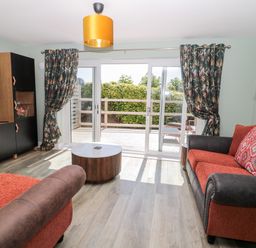 A living room with two red and brown sofas a round wooden coffee table floral curtains and sliding glass doors at Thrift Lodge in High Newton-by-the-Sea near Embleton