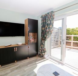 A living room with a wall-mounted TV cabinet and sliding glass doors leading to a wooden deck at Thrift Lodge in High Newton-by-the-Sea near Embleton
