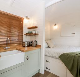 A small kitchen with wooden countertops next to a bed with a green blanket at Beech in Kemble