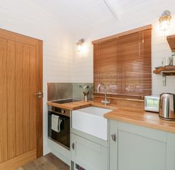 A kitchen with wooden door wooden countertop and wooden blinds on the window at Beech in Kemble
