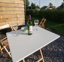 A white outdoor table with two wooden folding chairs a bottle of wine two wine glasses and a bowl on a stone-covered patio at Beech in Kemble