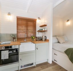 A small kitchen area with wooden countertop and sink next to a bed with patterned bedding and a green blanket at Hazel Kemble