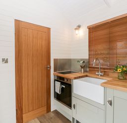 A kitchen with a wooden door a sink oven and utensils on the counter at Hazel in Kemble