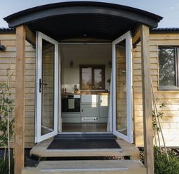 An open door showing a kitchen with cabinets and a window in a wooden small house at Hazel in Kemble